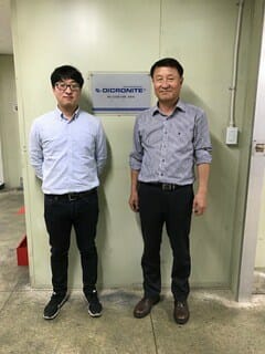 two men right in front of a company wall plaque