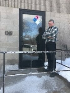 a man standing outside his building door with snow on the ground